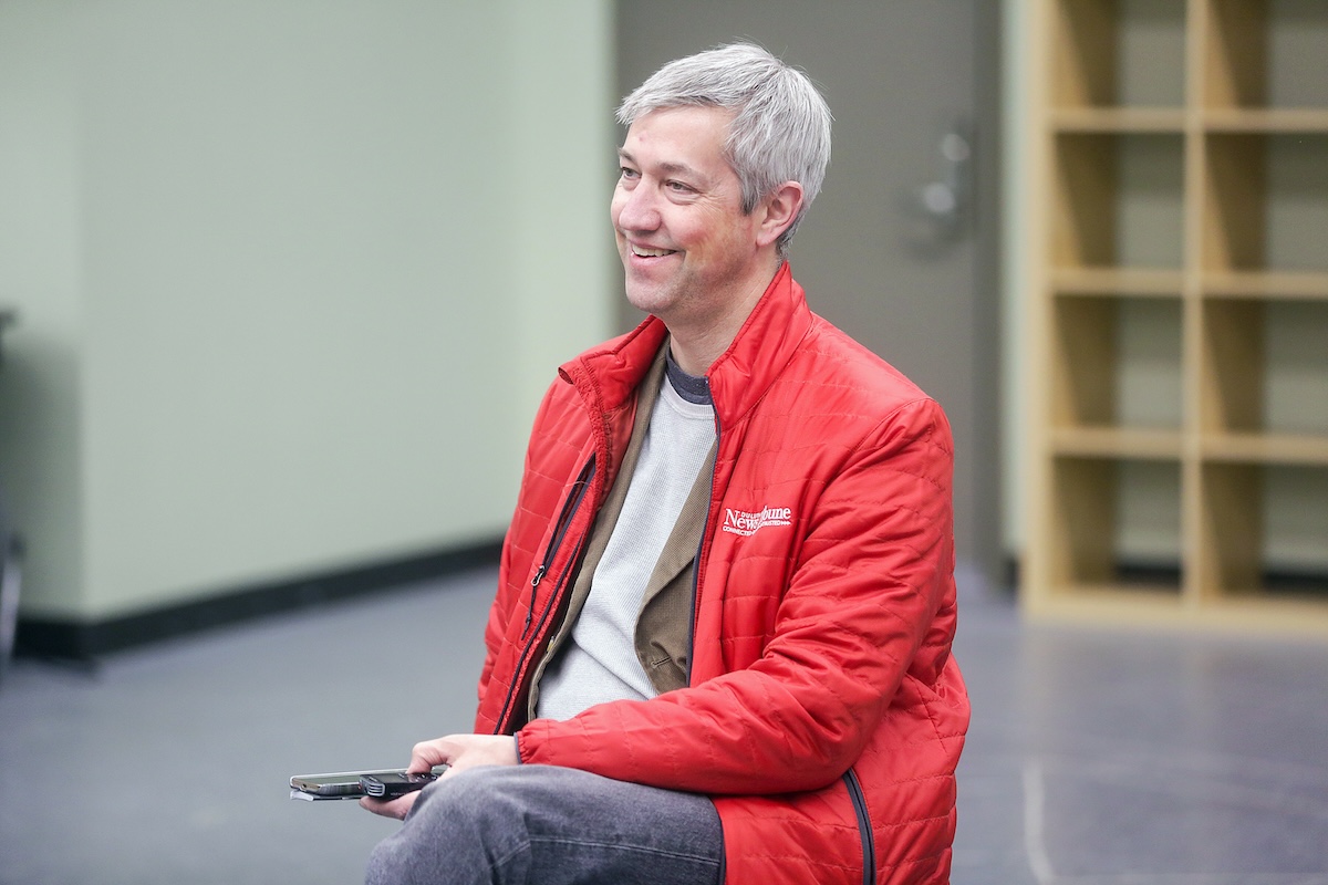 White man of 50 smiles while seated in a rehearsal room.